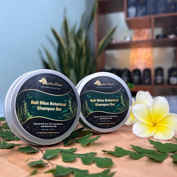 A round tin of Bali Bliss Botanical Shampoo Bar placed near a serene poolside, with tropical flowers beside it. The green label highlights tea tree, lemongrass, and rosemary oils, emphasizing its natural cleansing and nourishing properties.