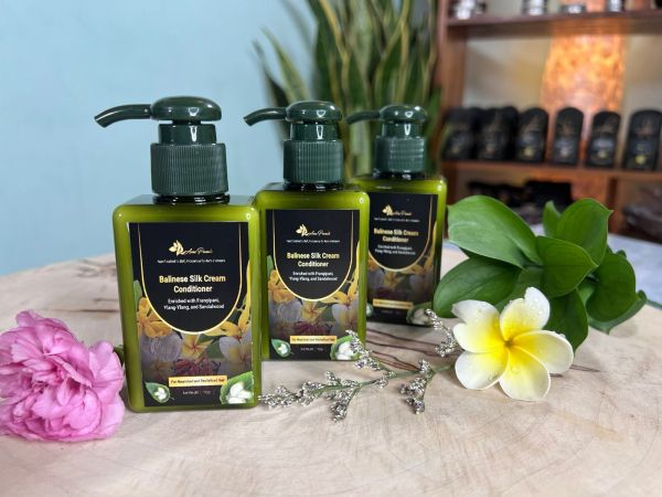 A sleek green bottle of Balinese Silk Cream Conditioner with a pump dispenser, set against a natural Balinese-inspired backdrop. The label highlights key ingredients like frangipani, ylang-ylang, and sandalwood for nourished and revitalized hair